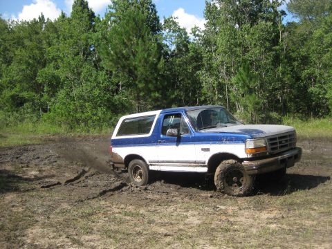 1994 Ford Bronco - A blue and white Ford Bronco navigates a muddy off-road trail.