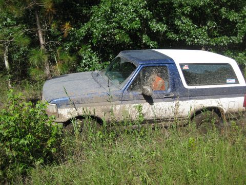 1994 Ford Bronco - A muddy Ford Bronco navigates through overgrown terrain.