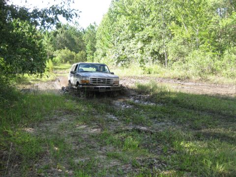 1994 Ford Bronco - A 1994 Ford Bronco navigates a muddy trail, kicking up water and dirt.