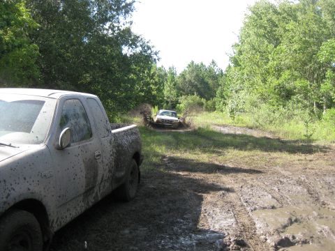 1994 Ford Bronco - Two trucks are off-roading through a muddy track in a wooded area.