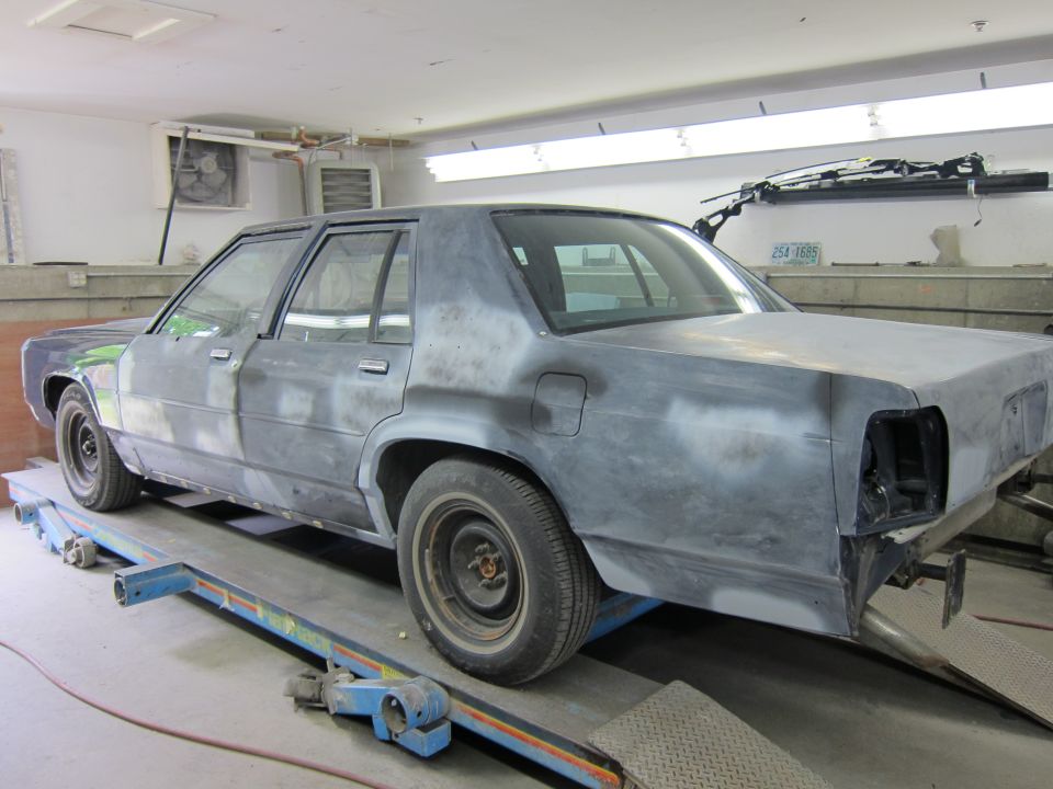 Gray sedan in a garage, rear quarter view, undergoing bodywork