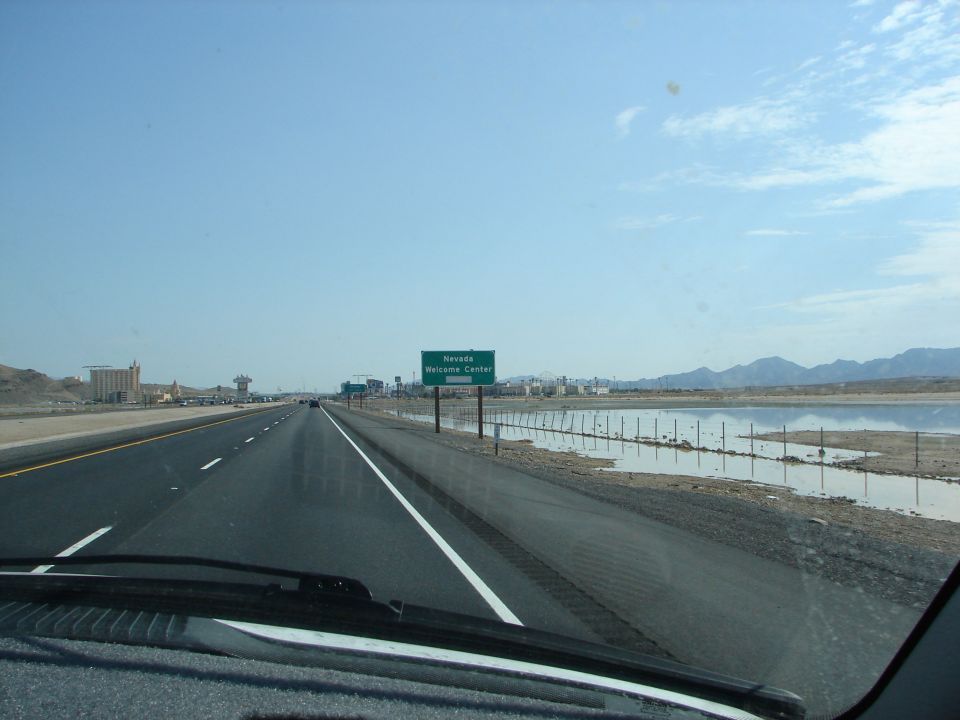 Highway view approaching Nevada Welcome Center sign with dry lake bed on the right