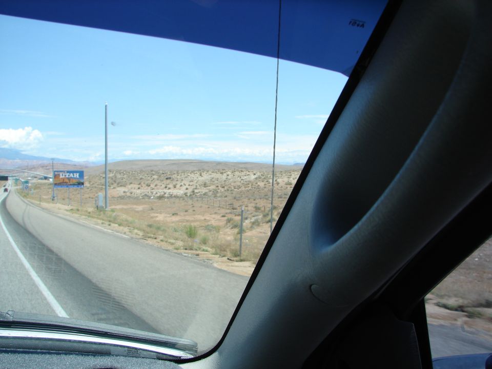 Interior pillar and windshield view of a highway in a desert landscape with a "UTAH" billboard