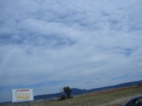 1992 Ford Taurus - Sign for South Dakota Mount Rushmore faces against a cloudy sky and rolling hills.