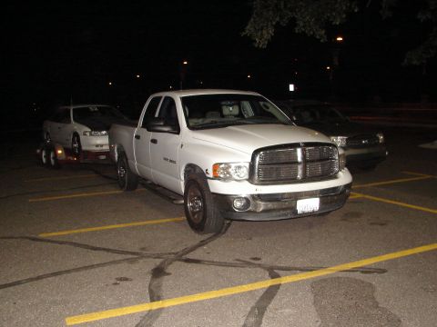 1992 Ford Taurus - A white Dodge Ram pickup truck is parked at night, towing a white car on a trailer.