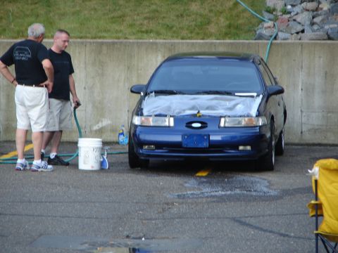 1992 Ford Taurus - A blue 1992 Ford Taurus is parked with its hood covered, as two men stand beside it.