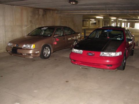 1992 Ford Taurus - Two Ford Taurus sedans, a red one with a black hood and a tan one, are parked side-by-side in a garage.