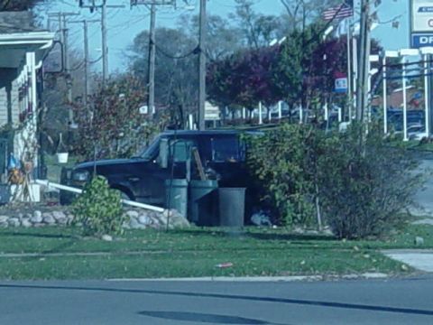 1992 Ford Bronco - A dark SUV is parked on the side of the road, surrounded by overgrown bushes and landscaping.