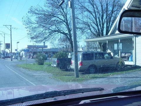 1992 Ford Bronco - SUV and pickup truck parked near a house with a gas station in the background.