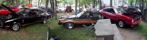 1978 Ford Mustang II - Two Ford Mustang IIs, one black with gold Cobra stripes and one red, are displayed at an outdoor car show.