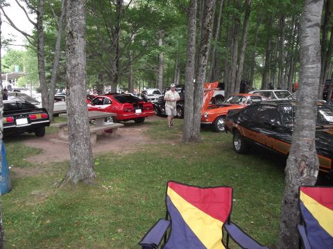 1978 Ford Mustang II - Several classic cars are on display in a wooded area at a car show.