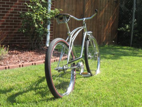 1994 Ford Bronco - A shiny chrome cruiser bicycle with red-striped tires is parked on a grassy lawn in front of a wooden fence.