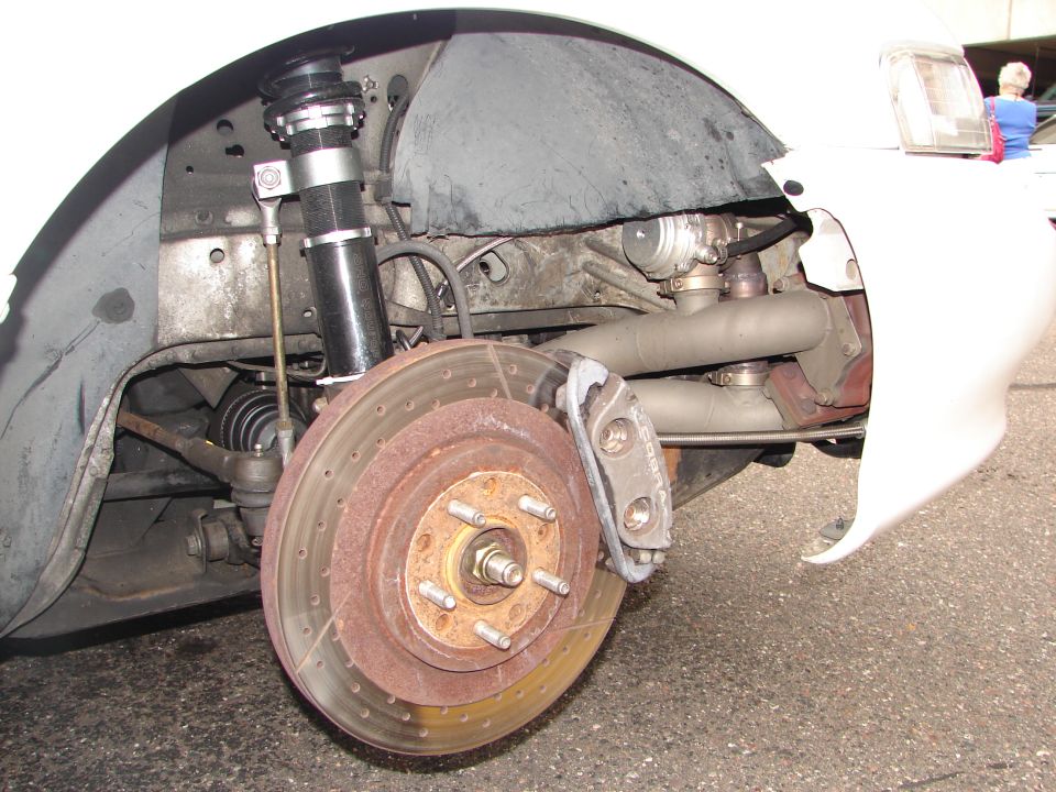 Car's front wheel, brake rotor, caliper, and suspension components are visible. The wheel well liner and part of the car's body are also in the shot