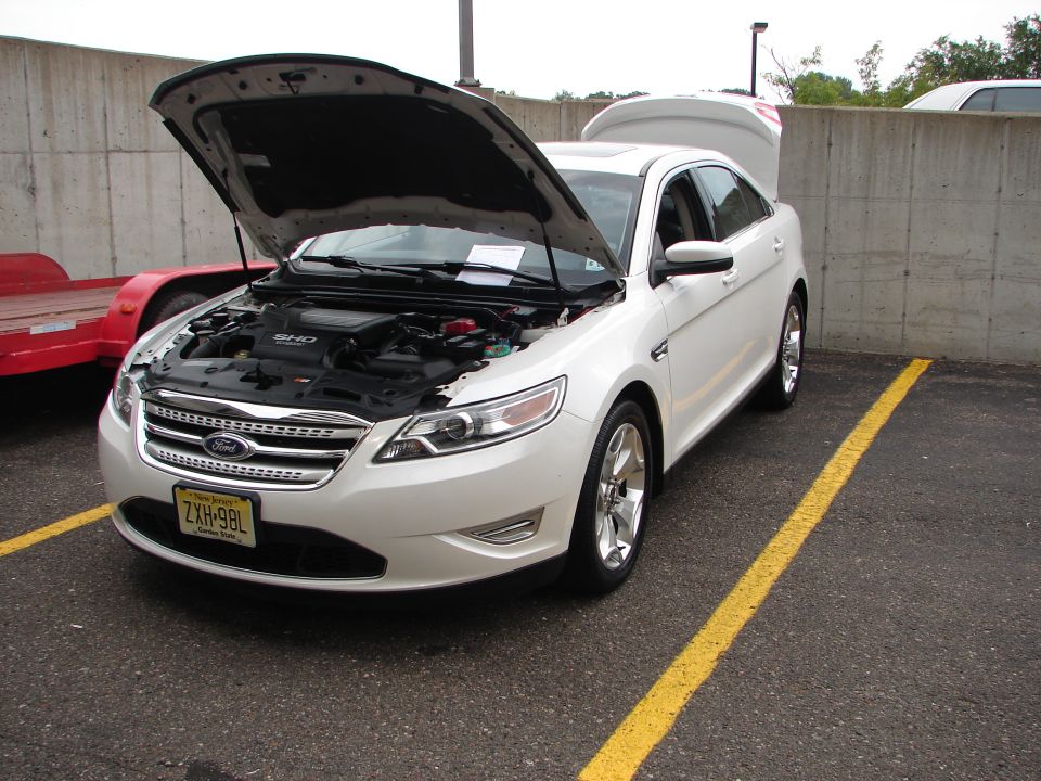 White Ford Taurus SHO with hood and trunk open, parked in a lot