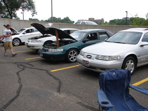 1992 Ford Taurus - Multiple Ford Taurus sedans are parked in a lot, with some hoods open, suggesting a car show or meet-up.