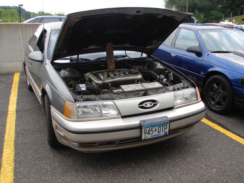 1992 Ford Taurus - The front of a 1992 Ford Taurus SHO is shown with its hood open, revealing the engine bay.