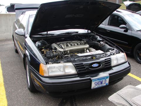 1992 Ford Taurus - A 1992 Ford Taurus SHO is displayed with its hood open, revealing the engine. Another black car is visible to the right.