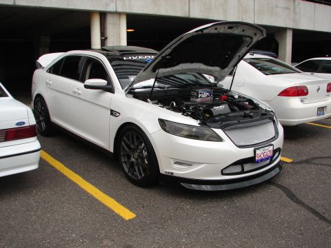 1992 Ford Taurus - A white sedan, likely a Ford Taurus from the 2010s, is parked with its hood open, revealing the engine compartment.