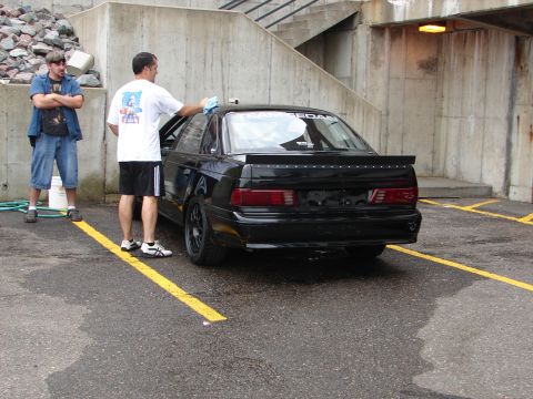 1992 Ford Taurus - A man wipes down the rear of a black 1992 Ford Taurus sedan while another man watches.