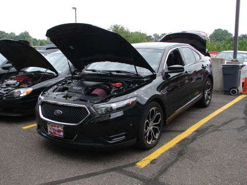 1992 Ford Taurus - A black sedan, identified as a 2013 model by its body style and SHO badging, is displayed with its hood open at an event.