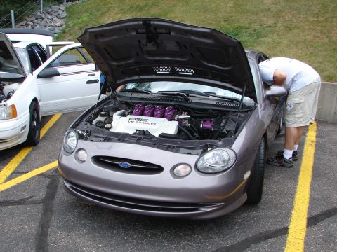 1992 Ford Taurus - A person inspects the engine of a gray Ford Taurus, parked next to a white car.