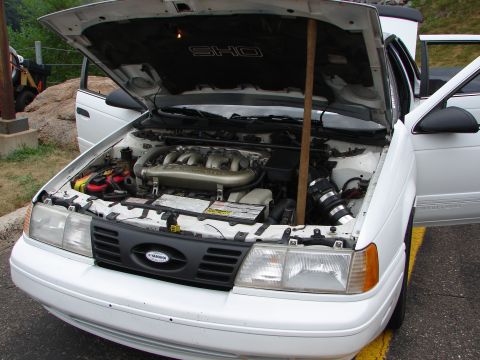 1992 Ford Taurus - The front of a white 1992 Ford Taurus is visible, with its hood open to reveal the engine compartment and SHO badging.