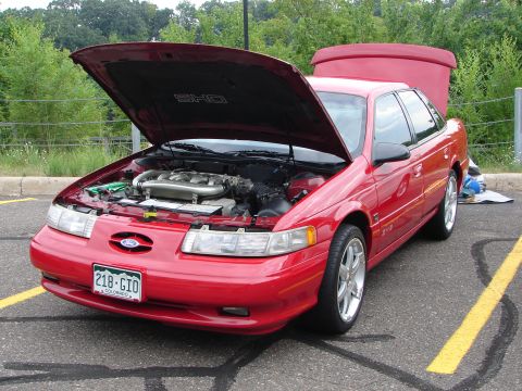 1992 Ford Taurus - A red 1992 Ford Taurus SHO is parked with its hood and trunk open, revealing the engine compartment.