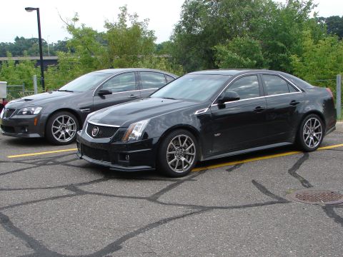 1992 Ford Taurus - Two sedans, a black Cadillac CTS and a gray Pontiac G8, are parked side-by-side in an asphalt lot.