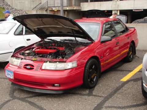 1992 Ford Taurus - A red 1992 Ford Taurus is parked with its hood open, revealing the engine bay. Another vehicle is visible to the left.