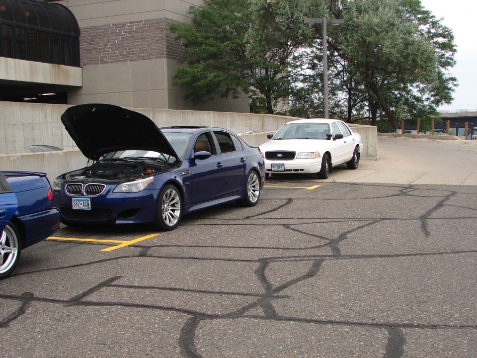 Blue sedan with hood open, parked next to a white sedan in a parking lot