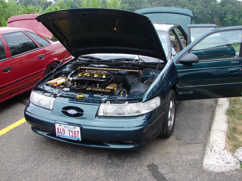 Green 1992 Ford Taurus, hood and driver door open, showing engine. Red car behind it