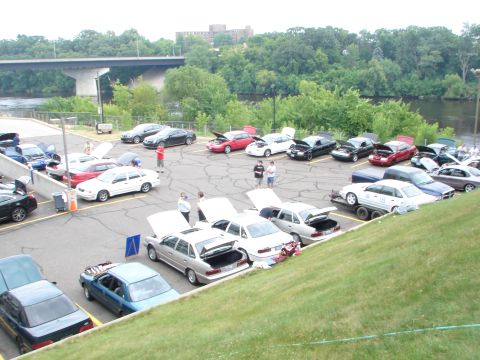 1992 Ford Taurus - A gathering of sedans in a parking lot by a river, with a bridge in the distance.