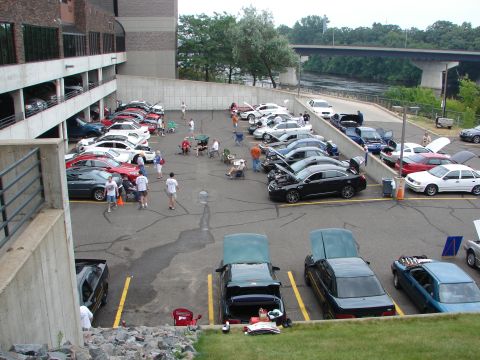 1992 Ford Taurus - A gathering of vehicles in a parking lot, with several hoods open, near a river and bridge.