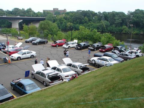 1992 Ford Taurus - A gathering of Ford Taurus sedans, some with hoods and trunks open, parked in an outdoor lot near a body of water.