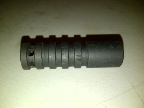1989 Ford Bronco - A black metal part with a ridged body and two visible holes on one end is shown against a light-colored surface.