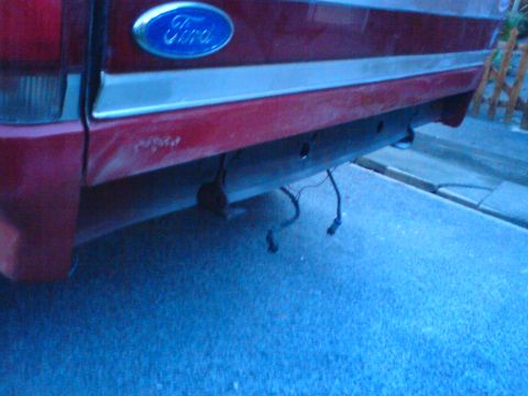 1989 Ford Bronco - The rear of a red 1989 Ford Bronco shows a dented bumper and dangling wires.