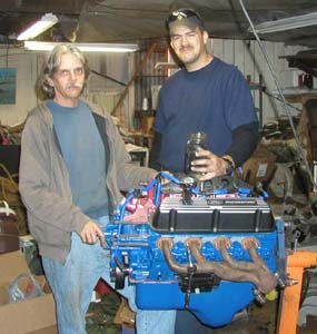 1988 Ford Bronco - Two men pose with a blue engine in a workshop setting.