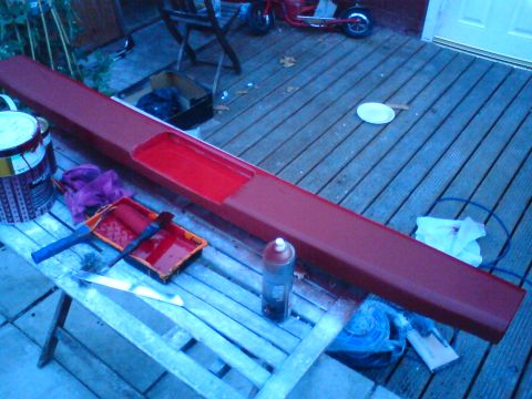 1989 Ford Bronco - A red car part is being painted on a wooden deck with various painting supplies nearby.