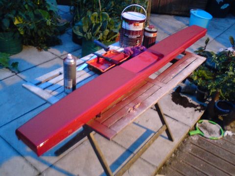 1989 Ford Bronco - A red painted car part rests on a table, surrounded by paint cans, rollers, and spray paint.