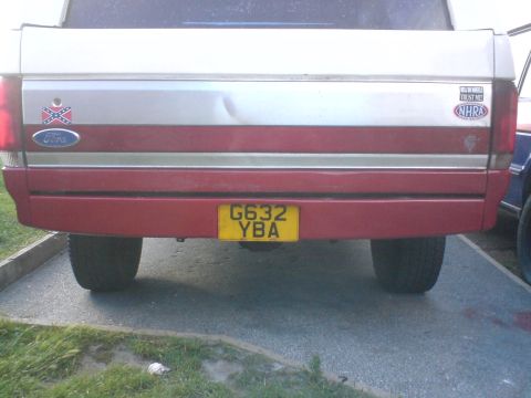 1989 Ford Bronco - The rear of a Ford Bronco shows a dent on the tailgate and various stickers.