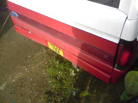 1989 Ford Bronco - The rear of a red and white vehicle is visible, with a damaged bumper and a yellow license plate.