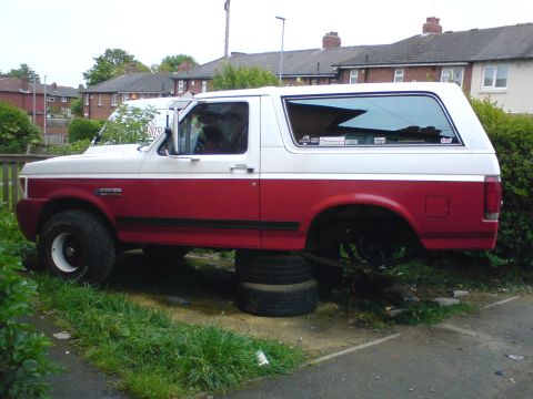1989 Ford Bronco - This two-tone red and white Ford Bronco is missing its rear tires and is propped up on stacked tires.
