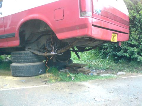 1989 Ford Bronco - The rear axle and leaf springs of a red truck are visible, supported by stacked tires.