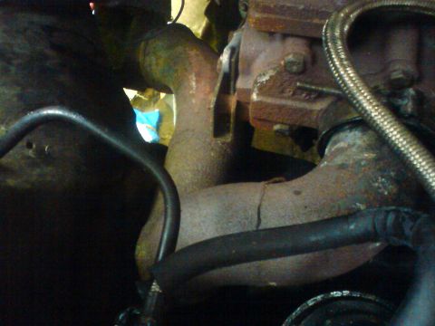 1989 Ford Bronco - The image shows a close-up view of rusty exhaust pipes and engine components, with some hoses visible.