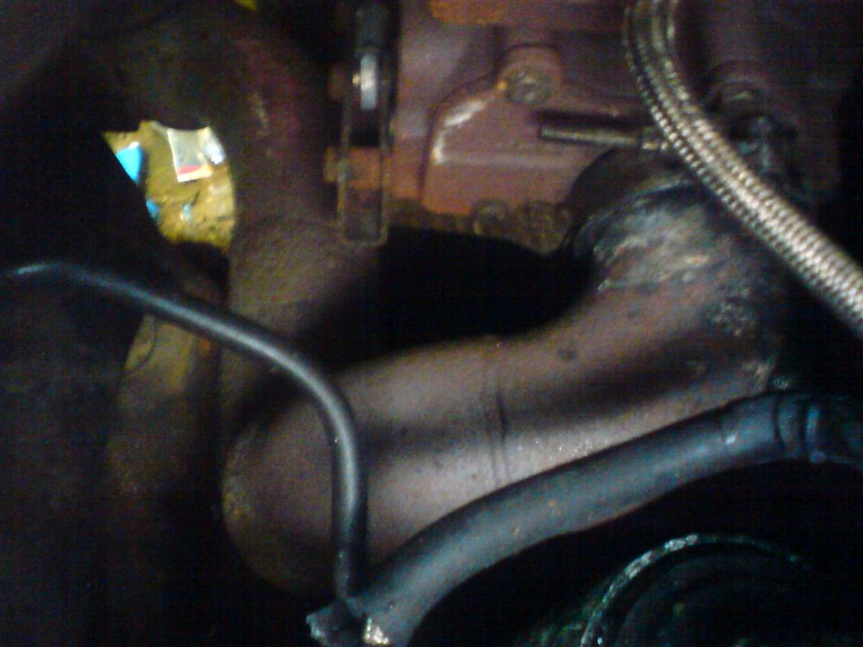 Engine exhaust manifold and metal piping with black hoses, dark interior