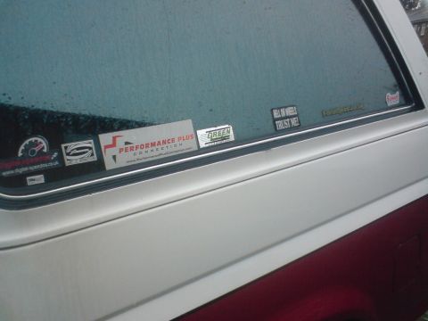 1989 Ford Bronco - A close-up view of a vehicle's side window, adorned with various stickers and showing signs of rain.