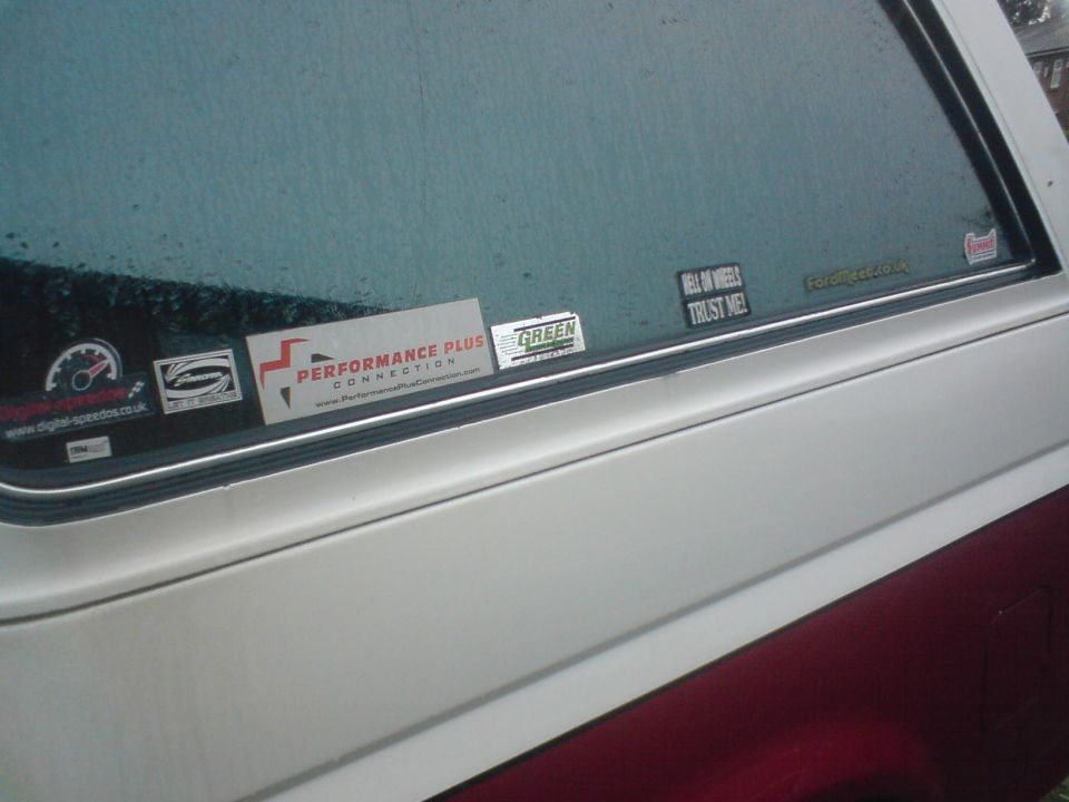 Side window of a vehicle with several stickers, including 'Performance Plus Connection' and 'Hell On Wheels Trust Me'