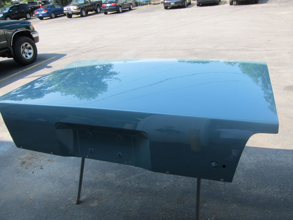 Teal car trunk lid on a stand, with reflections of trees and sky