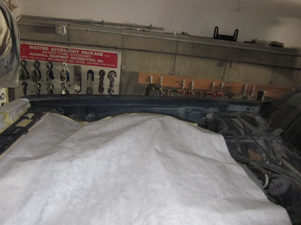 Car engine bay with a white cover over part of it. A sign with 'MASTER ACCESSORY PACKAGE' is on the wall above
