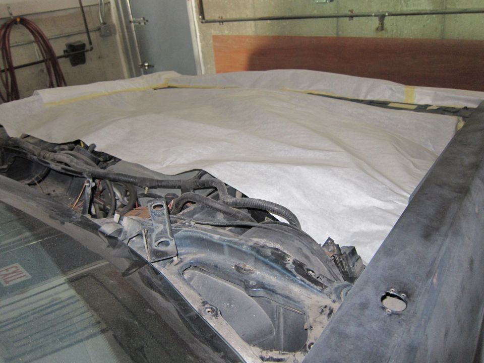 Car hood and engine bay covered with white protective material. Wires and some engine components are visible